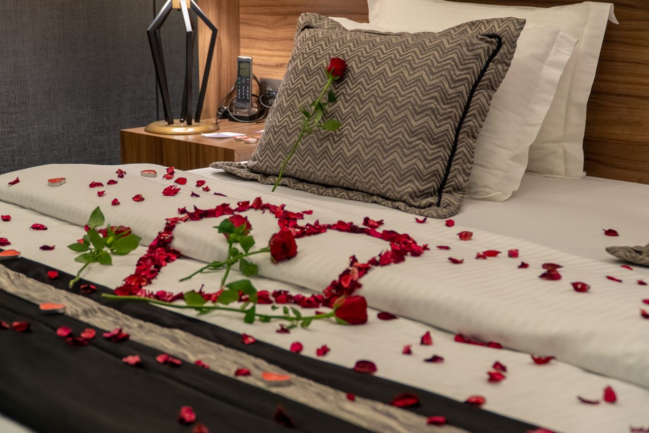 Hotel bed dressed with roses, linen and a wooden nightstand lamp