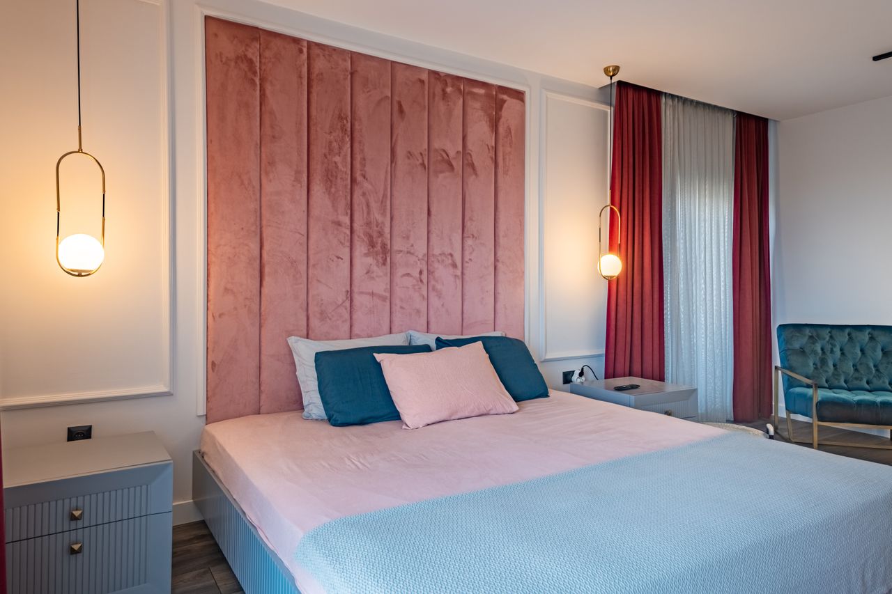 Fløyelssuite med høy rosa sengegavl og turkis lenestol